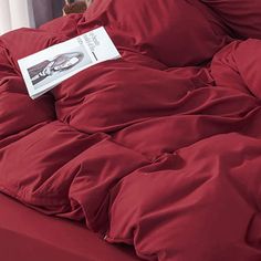 a red comforter is on top of a bed with a white sheet and pillow