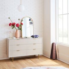 a white dresser sitting next to a window with flowers on it and a mirror above it