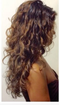 the back of a woman's head with long curly hair in front of a white wall