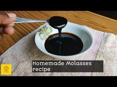 a person is spooning some black liquid into a white bowl on a wooden table