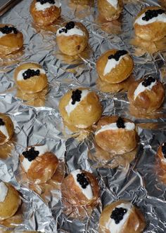 many pastries are on aluminum foil with black cavias and cream toppings