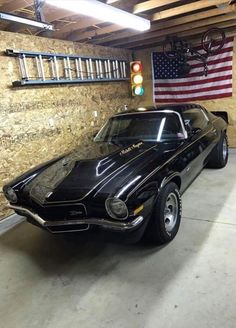 an old muscle car parked in a garage next to a wall with american flag on it