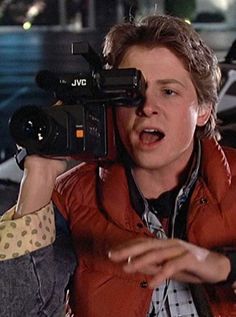 a young man holding a camera up to his face while sitting in front of a car