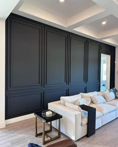 a living room filled with white furniture and black paneling on the wall behind it