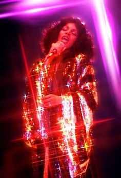 a woman singing into a microphone in front of bright lights and sparkles on the floor