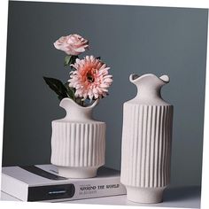 two white vases with pink flowers in them sitting on top of a stack of books