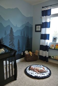 a baby is laying on the floor next to a crib in front of a mountain mural