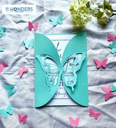 a blue and pink butterfly wedding card on a sheet of paper with white flowers in the background