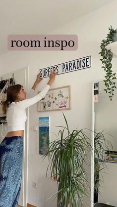 a woman in white shirt and blue skirt standing next to a sign that reads room inspo