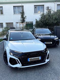 two white cars parked next to each other in front of a building with black doors