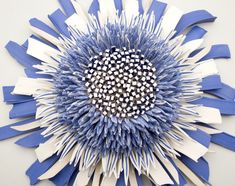 a blue and white flower made out of strips of paper on a wall in the shape of a sunflower