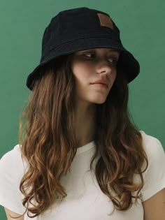 a woman with long hair wearing a black hat and white t - shirt against a green background