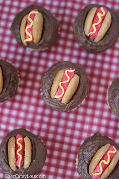 chocolate cupcakes with frosting and hotdog on them sitting on a red checkered tablecloth