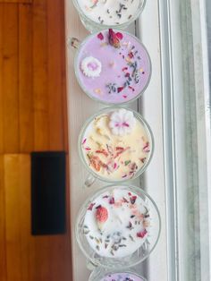 four desserts are arranged in glass bowls on a window sill with flowers and petals