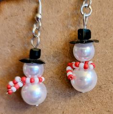 two snowmen wearing hats and candy canes are hanging from silver earwires