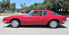 a red sports car parked in a parking lot next to a black fence and trees