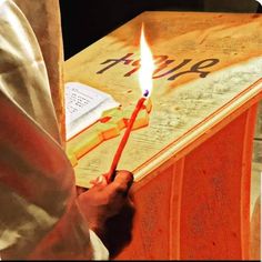 a person holding a lit candle in front of an open book