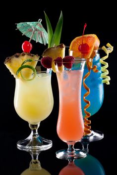 three different types of cocktails in glasses on a reflective surface with black back ground