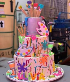 a multi - tiered birthday cake decorated with paint splatters and pencils