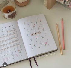 an open notebook sitting on top of a table next to a cup of tea and pencils