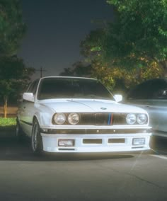 two cars parked next to each other in a parking lot with trees and bushes behind them