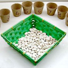 a green basket filled with white beans next to small cups and numbers on the table