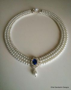 a necklace with pearls and a blue stone on the clasp is sitting on a white surface