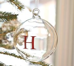 a glass ornament with the letter h hanging from a christmas tree in front of a window