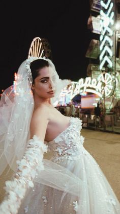 a woman wearing a wedding dress and veil standing in front of a carnival ride at night