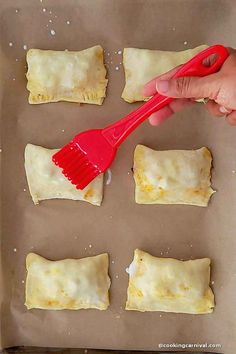 someone is using a red spatula to spread cheese on pastries in the baking pan