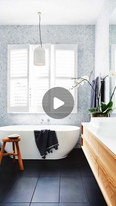 a white bath tub sitting in a bathroom next to a wooden stool and window with shutters