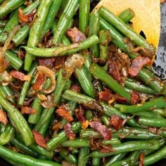 green beans with bacon and onions cooking in a skillet on the stove top next to a wooden spoon