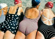 four women in bathing suits are sitting on the beach and one is wearing a blue hat