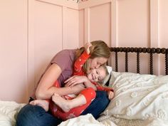 a mother and her daughter cuddle on the bed in their pink bedroom at home