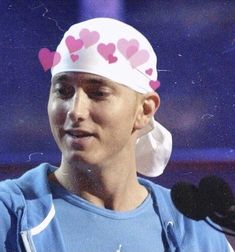 a woman wearing a pink and white hat with hearts on it's head while standing in front of a microphone