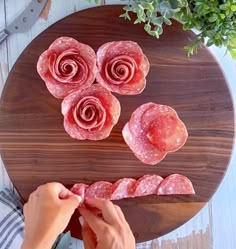 a person cutting up slices of salami on a wooden board