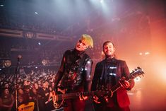 two men standing next to each other on stage with guitars in front of an audience