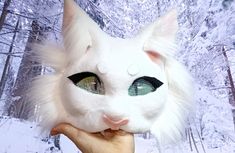 a person holding up a white cat's face in front of a snowy forest