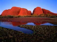 the mountains are red and there is a small pond in front of them that has water running through it