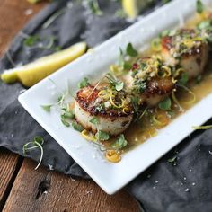 a white plate topped with scallops covered in sauce and garnished with herbs