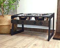 two metal bowls with paw prints on them are sitting on a wooden table next to a potted plant