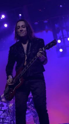 a man with long hair playing guitar in front of purple lights at a music concert