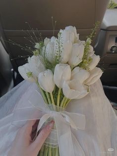 a bouquet of white tulips in a vase on the back seat of a car