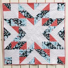 a quilted wall hanging on the side of a white building with red and blue accents