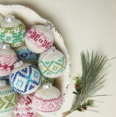 a white bowl filled with knitted ornaments next to a pine branch and twig