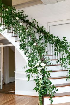 the stairs are decorated with greenery and white roses on them, along with wood flooring