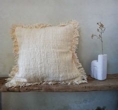 a white pillow sitting on top of a wooden shelf next to a vase with a plant