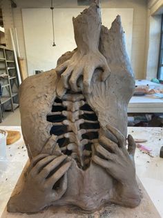 a clay sculpture of a human skeleton with hands on it's back, in the process of being made