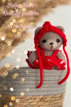 a knitted teddy bear wearing a red hat and scarf sitting on top of a basket