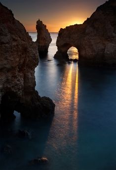 the sun is setting over the ocean and rocks in the water, with an arch shaped rock formation